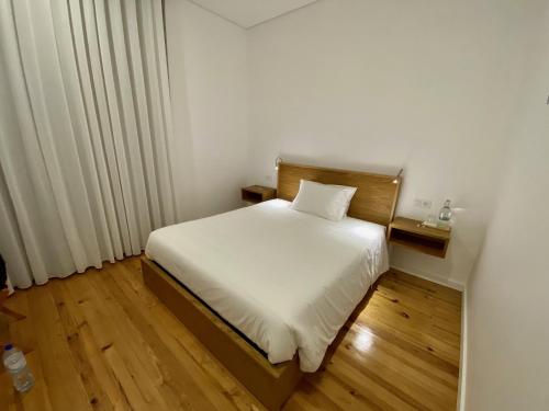 um quarto com uma cama branca e piso em madeira em DOURO B&B Avenida em Resende