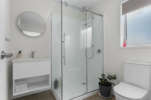 a white bathroom with a shower and a toilet at Marram Studio - Mangawhai Holiday Studio in Mangawhai