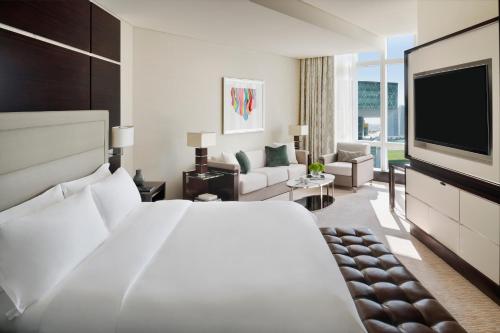 a bedroom with a large white bed and a living room at Rosewood Abu Dhabi in Abu Dhabi