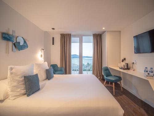 um quarto de hotel com uma grande cama branca e uma secretária em Côté Thalasso Hôtel & Spa Marin em Banyuls-sur-Mer