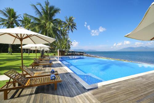 a swimming pool with chairs and umbrellas next to the ocean at Villa So Long Banyuwangi - Ijen in Banyuwangi