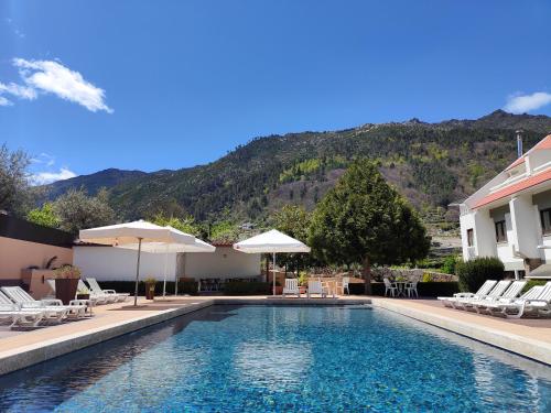 a swimming pool with chairs and umbrellas next to a building at Hotel Berne in Manteigas