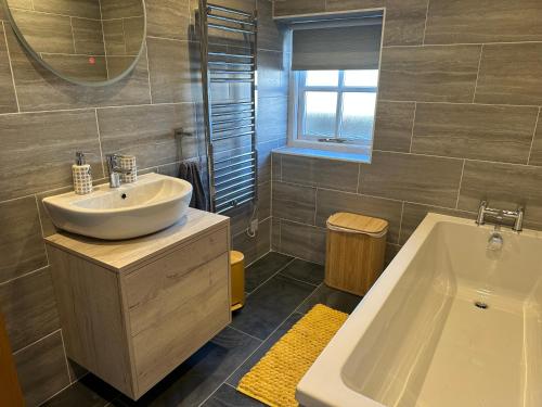 a bathroom with a sink and a tub and a mirror at Beudy Howel - A beautiful converted barn close to the coast in Llansadurnen