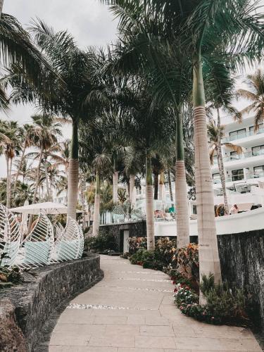 a walkway with palm trees and a building at Hotel Fariones in Puerto del Carmen