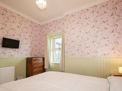 1 dormitorio con papel pintado de color rosa, cama y ventana en Station House en Lybster