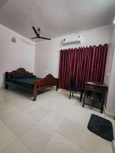 a bedroom with a bed and a desk and a red curtain at Urban Haven Short Stays in Trivandrum