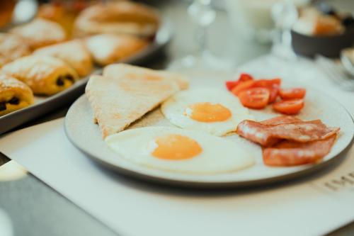 a plate of eggs and ham on a table with pastries at Impero Nafplio Hotel & Suites in Nafplio