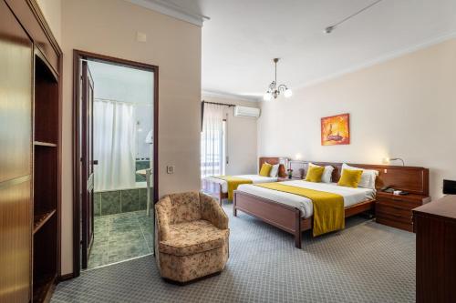 a hotel room with two beds and a chair at Hotel Colmeia in Monte Real