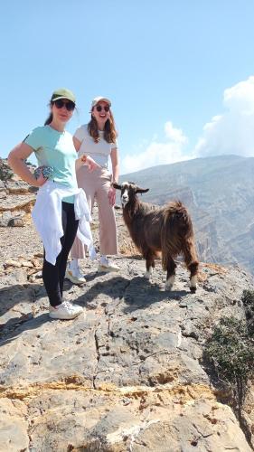 two women standing on top of a mountain with a goat at Sehma Guest House بيت السحمه للضيافه in Al Ḩamrāʼ