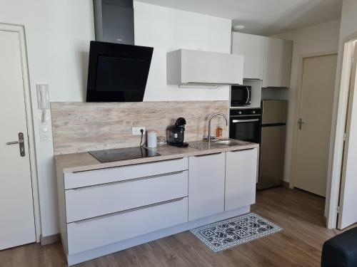 eine weiße Küche mit einer Spüle und einer Mikrowelle in der Unterkunft Saumur centre : appartement entièrement rénové. in Saumur