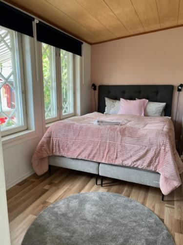 a bedroom with a bed with a pink blanket and two windows at Hotelli Kaivo in Naantali