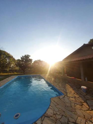 a blue swimming pool with the sun in the background at Chácara com Piscina in Araçoiaba da Serra
