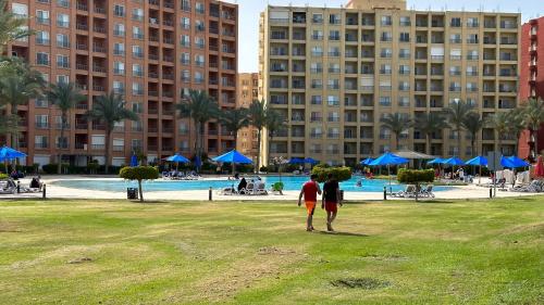 two people standing in a park in front of a pool at شاليه Aqua بورتو جولف مارينا in El Alamein