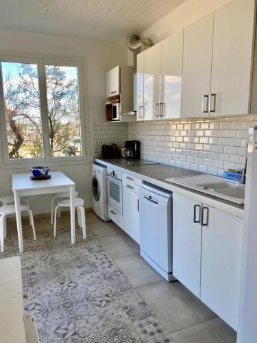 une cuisine avec des armoires blanches, une table et un évier dans l'établissement Chaleureuse villa sur la dune, à Mimizan