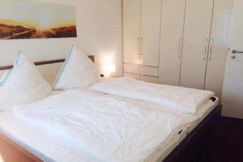een bed met witte lakens en kussens in een kamer bij Haus Belvedere App 13 Stellpl 70 in Grömitz