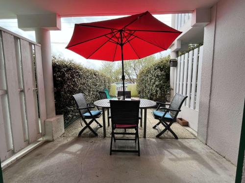 - une table et des chaises avec un parasol rouge sur la terrasse dans l'établissement Appartement 2 pièces - 4 pers - Terrasse - Proche Port de La Cotinière, Plage et Commerces - FR-1-246A-225, à La Cotinière