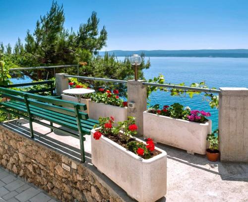 a green bench sitting next to some flowers and the water at Apartmani Lučica in Mimice
