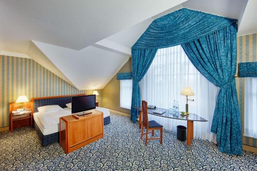 a hotel room with a bed and a desk and a television at Dorint Herrenkrug Parkhotel Magdeburg in Magdeburg