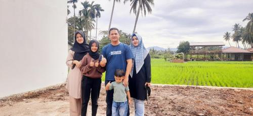 a family poses for a picture in front of a rice field at Wafaby Guest House in Payakumbuh