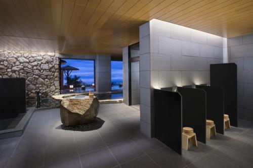ANA InterContinental Beppu Resort & Spa, an IHG Hotel في بيبو: حمام مع حوض استحمام وجدار حجري