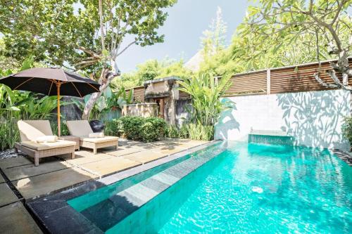 a pool with chairs and an umbrella next to a house at Mayaloka Villas in Seminyak