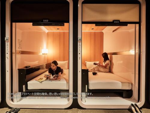 Dos personas sentadas en las camas en una habitación en First Cabin Nishi Umeda, en Osaka