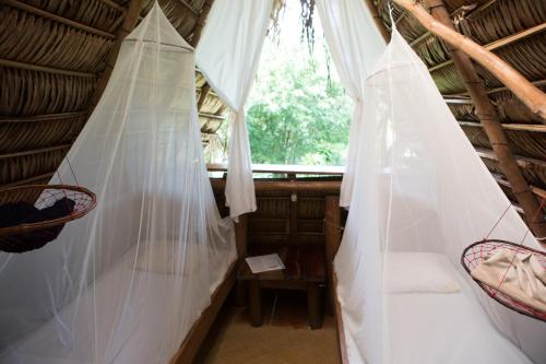 a room with a bed and curtains in a thatched room at El Hotelito Perdido in Rio Dulce