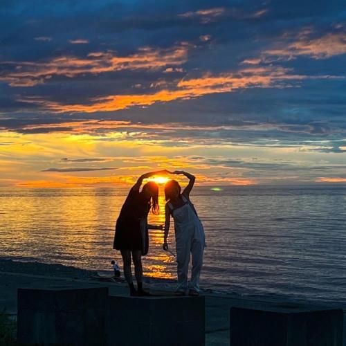 two women standing on the beach at sunset at ゲストハウス＆カフェ　ハレテル in Masuda
