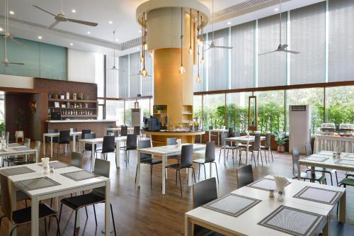 a restaurant with white tables and chairs and windows at Somerset Park Suanplu in Bangkok