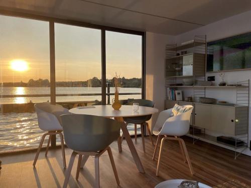 une salle à manger avec une table, des chaises et une grande fenêtre dans l'établissement Hausboot Fjord Schleiliebe mit Biosauna und Dachterrasse in Schleswig, à Schleswig