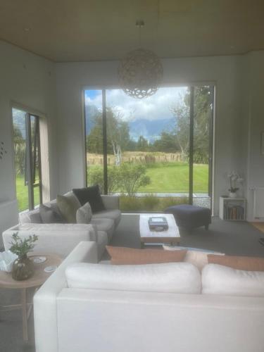 a living room with white furniture and a large window at Mathesons Escape in Fox Glacier
