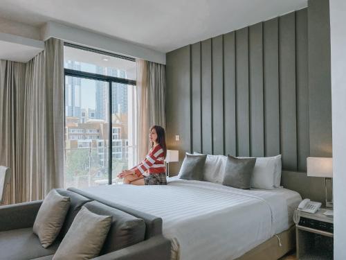 a woman sitting on a large bed in a hotel room at Arden Hotel and Residence by At Mind in Pattaya Central