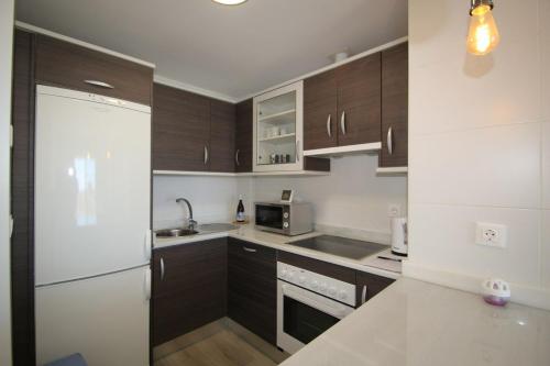 a kitchen with brown cabinets and a white refrigerator at Small Oasis Nelson Mandela Apartment with sea view, two bedrooms, parking, terrace and pool in Manilva
