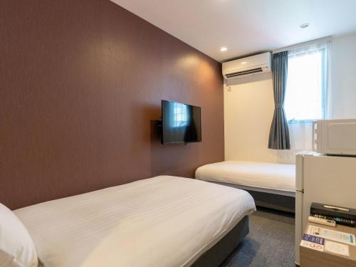 Zimmer mit 2 Betten und einem TV an der Wand in der Unterkunft HOTEL R9 The Yard Ashikagaekinishi in Ashikaga