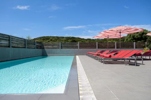 a swimming pool with red chairs and an umbrella at Le Golfe in Porto Pollo