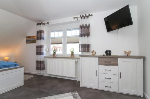 a kitchen with white cabinets and a flat screen tv at Ferienwohnungen Gatena in Norddeich