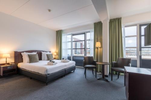 a bedroom with a bed and two chairs and windows at Amrâth Hotel Alkmaar in Alkmaar