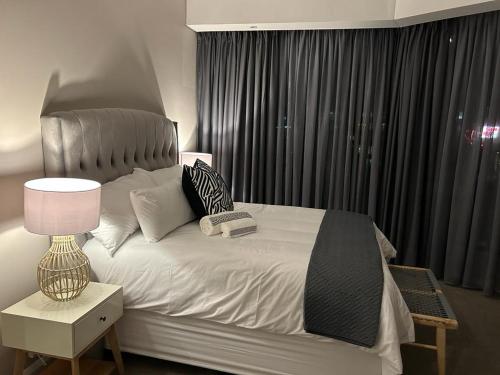 a bedroom with a bed with a lamp and a window at Triology Menlyn Maine Residences in Pretoria