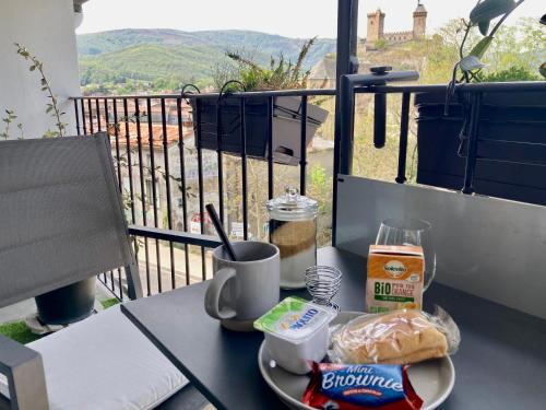einen Tisch mit einem Teller Essen auf dem Balkon in der Unterkunft Studio Le Roof - Une vue splendide - Petit déjeuner inclus 1ère nuit - AUX 4 LOGIS in Foix