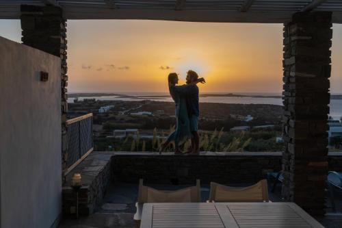 a statue of a couple standing on a balcony with the sunset at Anthemion Paros - Villas & Suites in Agia Irini Paros