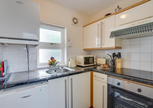 uma cozinha com armários brancos e um lavatório em Eluned Tresaith em Penbryn
