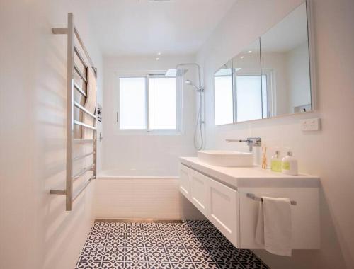 Baño blanco con lavabo y espejo en SALTY SNOOZE - Your Coastal Holiday House en Avalon