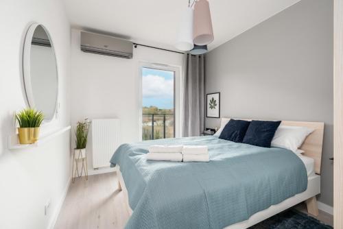 a white bedroom with a blue bed and a window at Stara Cegielnia Lake View Apartment by Renters Prestige in Poznań