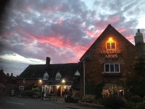 un edificio con un cartel que lee brazos de fuera al atardecer en College Arms en Stratford-upon-Avon