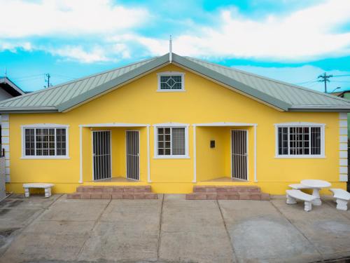 a yellow building with two benches in front of it at Kiskadee Korner Vacations in Buccoo