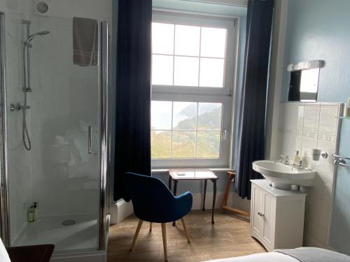 a bathroom with a shower and a blue chair and a sink at Sinai House in Lynton