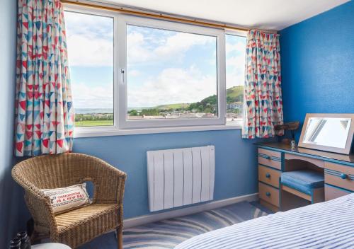 a bedroom with a bed and a chair and windows at Angorfa Aberaeron Apartment in Aberaeron