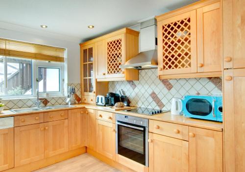 a kitchen with wooden cabinets and a blue microwave at Kookaburra in Abersoch