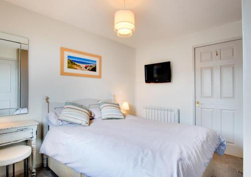 a bedroom with a white bed with a tv on the wall at Kookaburra in Abersoch