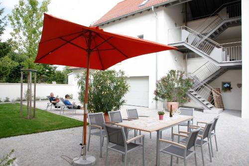 a table and chairs with a red umbrella on a patio at Gästehaus Vogler in Heuchelheim-Klingen